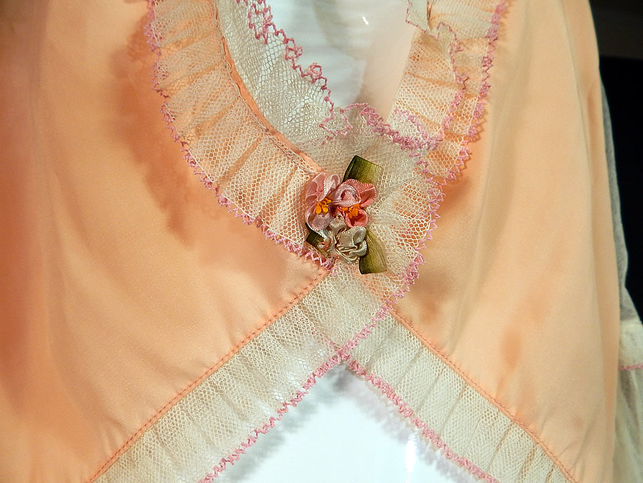 Vintage Pink Silk White Ruffle Rosette Trim Lingerie Boudoir Bed Jacket
This lovely lingerie boudoir bed jacket blouse top has a short crop cutaway style shorter in the front, longer in the back, with sheer 3/4 length sleeves, ruffle cuffs, an open front with a single snap closure hidden underneath the rosette trim at the waist and is sheer, unlined.