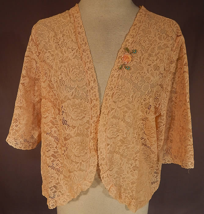 Vintage Silk Pastel Rosette Trim Cream Lace Bolero Boudoir Bed Jacket
This vintage silk pastel rosette trim cream lace bolero boudoir bed jacket dates from the 1930s. It is made of an off white cream color sheer lace fabric, with a floral leaf pattern and a small silk pastel ombre rosette ribbon work appliqu&eacute; trim sewn onto the lapel. 