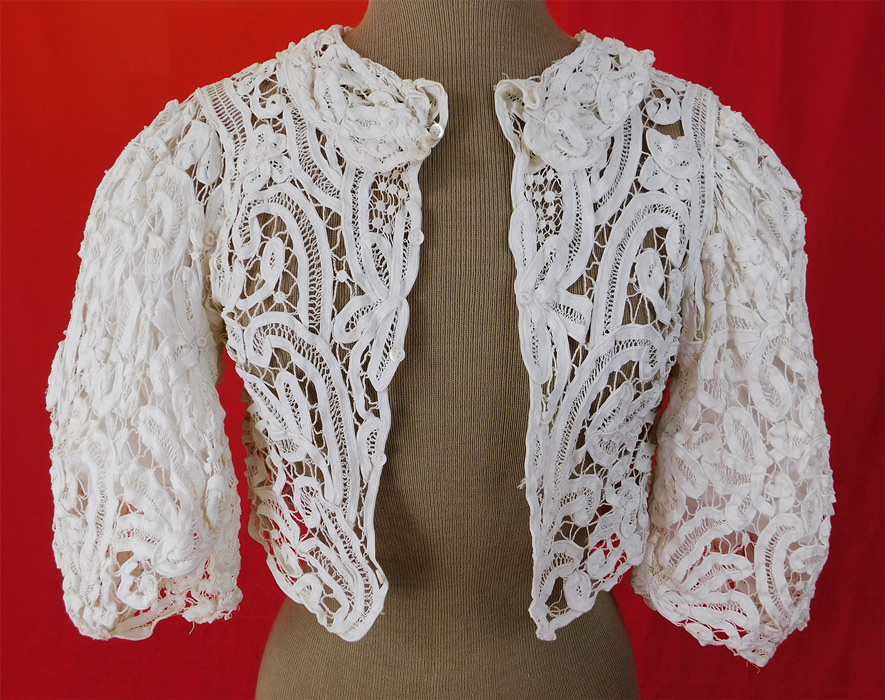 Victorian White Battenburg Tape Lace Short Crop Bodice Blouse Bolero Jacket
This exquisite antique Victorian era white battenburg tape lace short crop bodice blouse bolero jacket dates from 1900. It is made of a white hand made battenburg tape lace with connecting thread picot ornamented bars, buttonhole stitches and decorative spiral, floral, leaf, scroll work designs. 