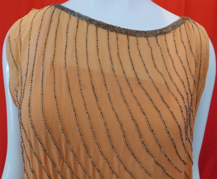 Vintage Art Deco Peach Silk Silver Beaded Grecian Goddess Style Flapper Dress
This fabulous flapper dress has a Grecian goddess gown asymmetrical style, with side gathering, a long draped beaded sash hanging down from one side, with side snap closures, is sleeveless and is fully lined with a peach silk slip sewn inside.
