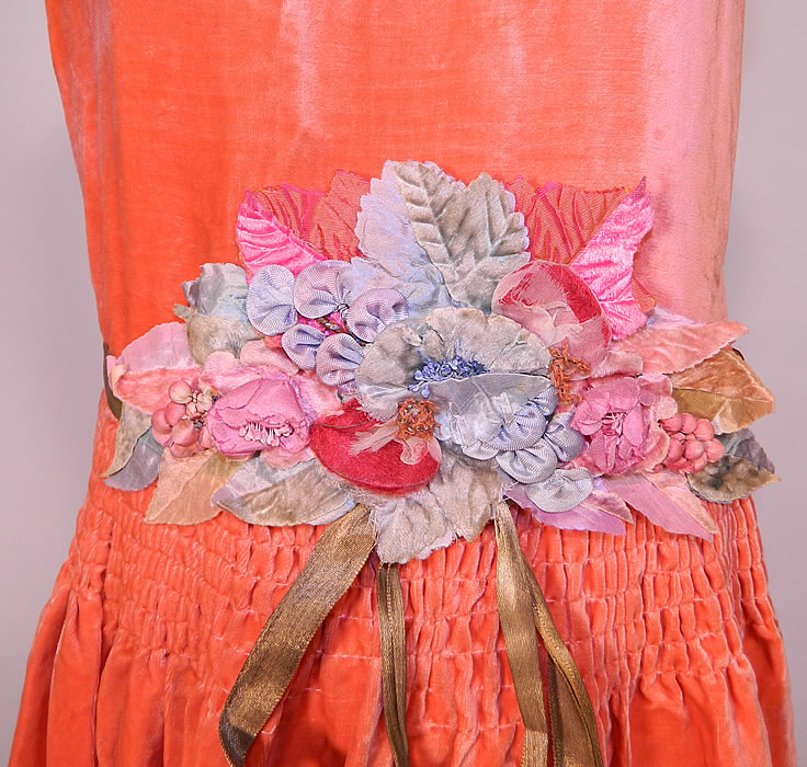 Vintage Coral Velvet Pastel Rosette Gold Lam&eacute; Ribbon Belted Drop Waist Flapper Dress. There is a gold lam&eacute; metallic ribbon sash belt with large pastel silk velvet rosette flower applique on front and mink fur trim edging the bottom skirt hemline. 