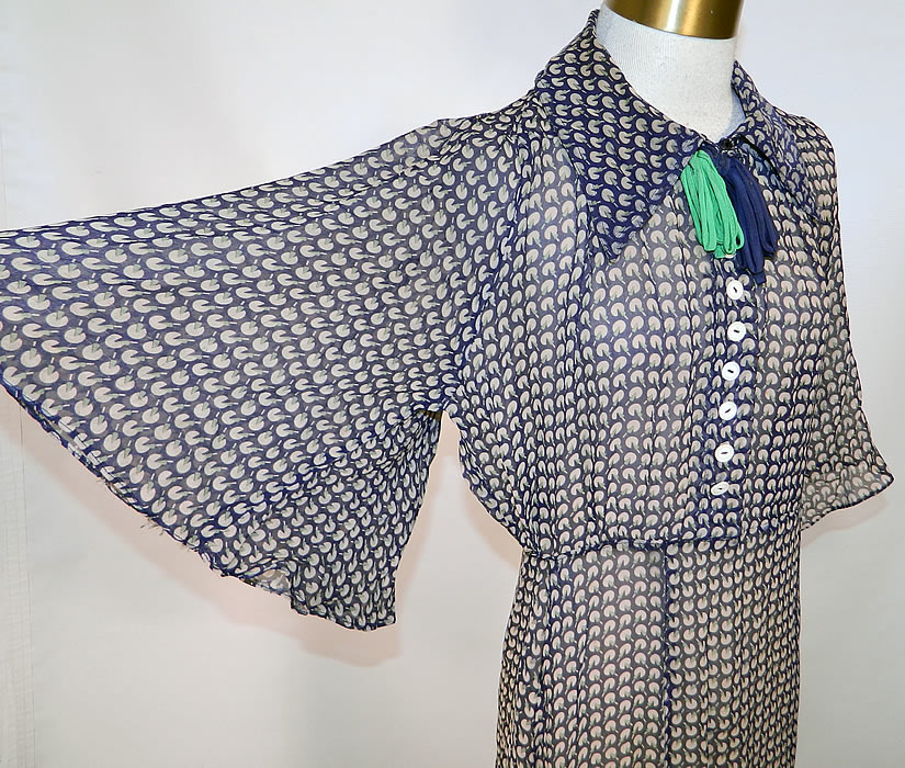 Vintage Blue & Green Silk Chiffon Novelty Print Batwing Sleeve Day Dress. This charming day dress is a long mid length, with a fold over collar, ribbon necktie trim, buttons down the front top, wide flared batwing sleeves, side snap closures and is sheer unlined. 