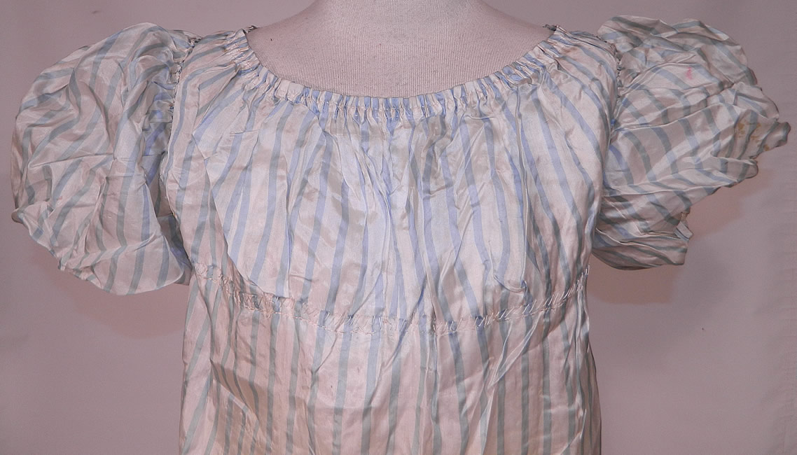 Antique Georgian Regency Era Blue & White Stripe Silk Puff Sleeve Girls Dress
It is hand stitched, made of a light periwinkle blue and white striped fine silk fabric. This gorgeous Georgian girls gown would have been worn by a young lady and has a high empire waist with gathered stitching which would have had drawstring closures around it and the neckline, puff balloon shape gigot sleeves and a ruffle bottom hem skirt. 