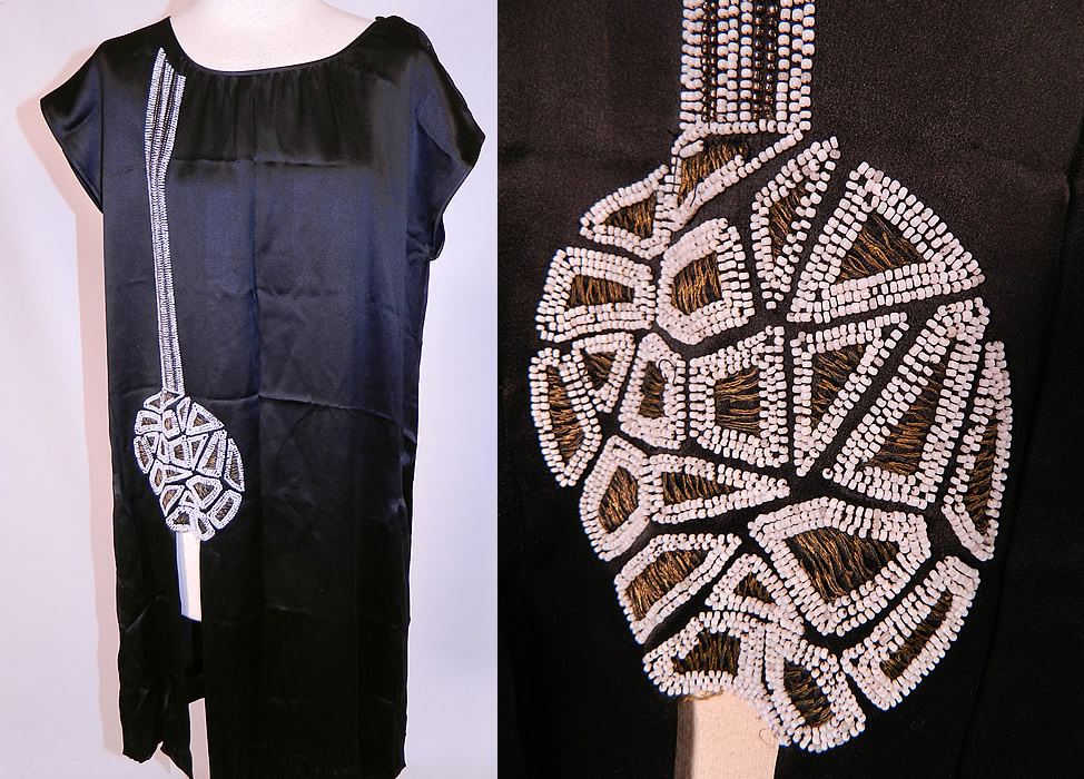 Vintage Art Deco Black Silk White Beaded Flapper Tunic Chemise Dress. 
This Art Deco vintage black silk white beaded flapper tunic chemise dress dates from the 1920s. It is made of a black silk satin fabric, with white beading and gold metallic thread embroidery work done in an Art Deco abstract circular geometric pieced puzzle design along the front side. 