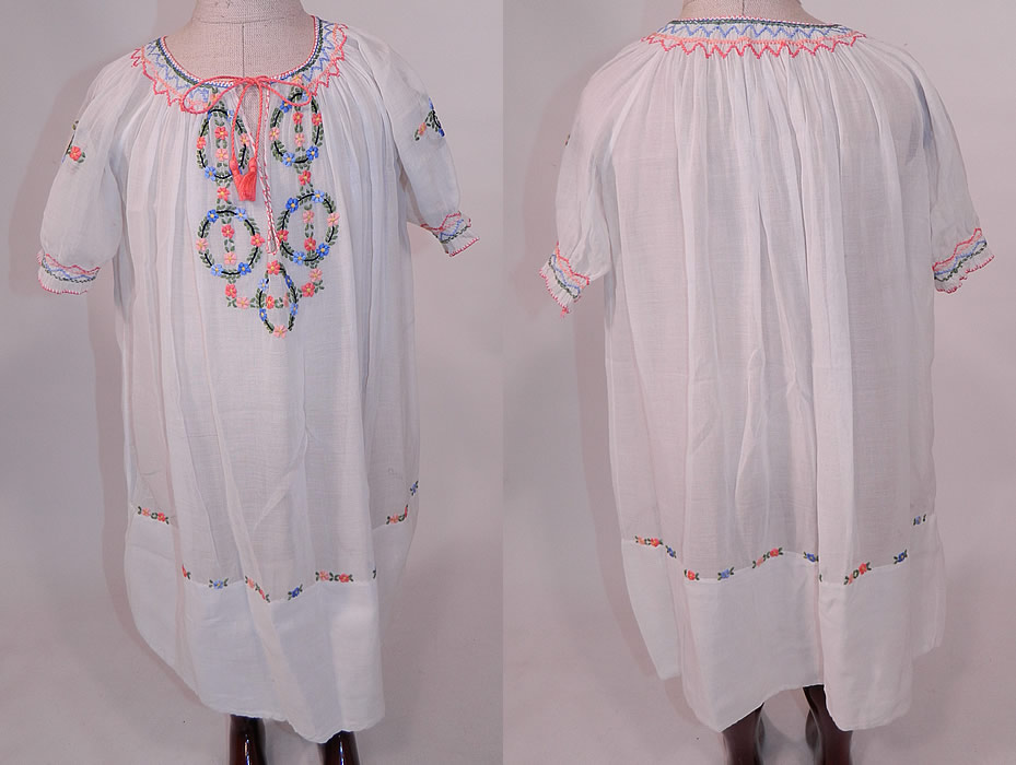 Vintage Childs White Cotton Colorful Embroidered Smocking Hungarian Peasant Dress
This vintage child's white cotton colorful embroidered smocking Hungarian peasant dress dates from the 1920s. It is made of a white sheer cotton batiste fabric, with colorful raised padded satin stitch hand embroidery work and smocking details with floral leaf rosette garland wreath designs.