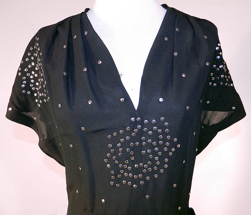 Vintage Black Silk Silver Metal Sequin Studded Beaded Cocktail Dress
This stunning studded cocktail dress has a V front neckline, short cap sleeves, a short mid length skirt with side hip drape gathering, a side zipper closure and is sheer, unlined. 