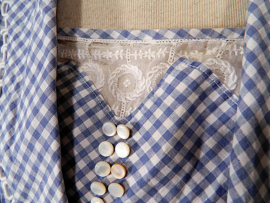 Edwardian Blue & White Gingham Check Cotton Pinafore Belted Day Dress
The dress has a slight drop waist, with snap closures along the front side, short sleeves with rolled cuffs and is unlined. There is a matching fabric pinafore, sleeveless overcoat, with fold over lapel collar and a belted front tie sash closure.
