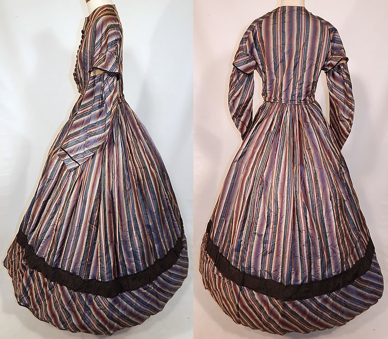 Victorian Civil War Era Purple & Blue Ombre Stripe Silk Hoop Skirt Gown Dress
This stunning striped dress has a long floor length full hoop skirt (hoop not included underneath), with attached fitted bodice top, long layered full sleeves, brown velvet trim, faux button trim with hidden hook closures underneath down the front, side skirt pockets with a bundle of extra dress fabric wrapped inside and is fully lined. 