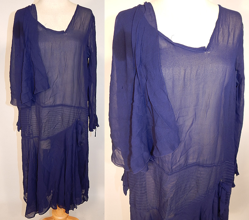 Vintage Art Deco Navy Blue Silk Chiffon Capelet Asymmetrical Drop Waist Dress
This vintage navy blue silk chiffon capelet asymmetrical drop waist dress dates from the 1920s. It is made of a navy blue sheer silk chiffon fabric, with decorative pleated stitching details. This delightful day dress is loose fitting, with a drop waist, shoulder capelet attached onto one side, an uneven asymmetrical neckline and skirt, front drape skirt panel with side bow trim, long sleeves and is sheer, unlined