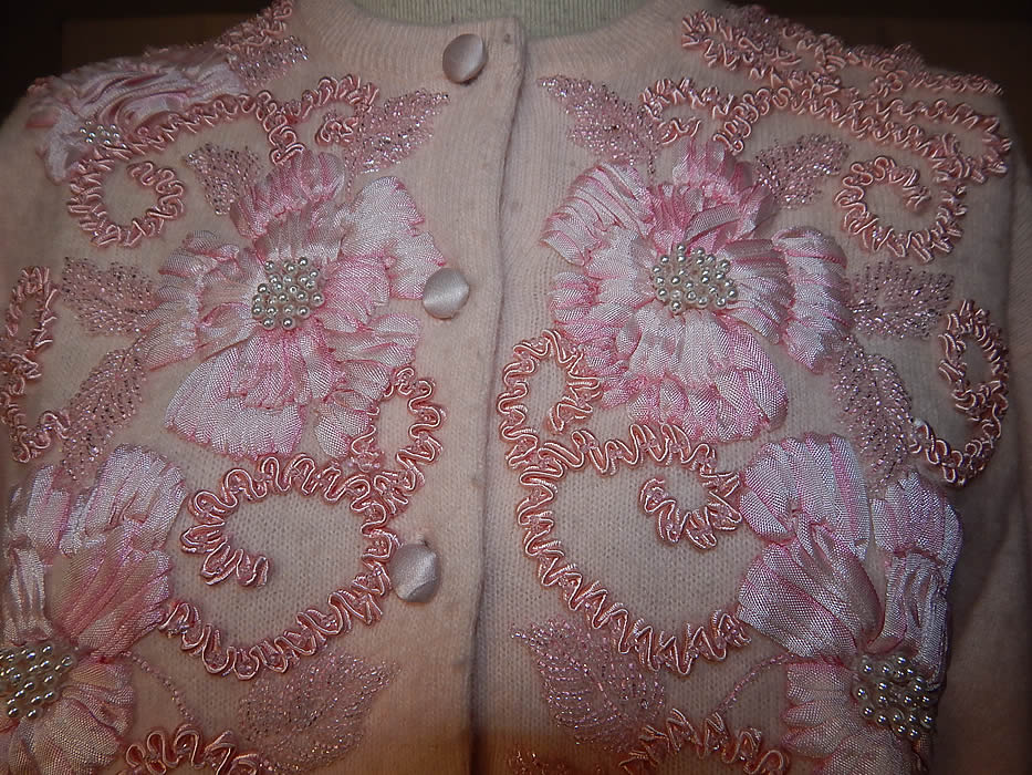 Vintage Oriental Galleries Hong Kong Pink Ribbon Work Beaded Sweater
This pretty pink cardigan sweater has a ribbed fitted waistband, cuffs, collar, long full sleeves, fully lined and pink silk buttons down the front for closure. 
