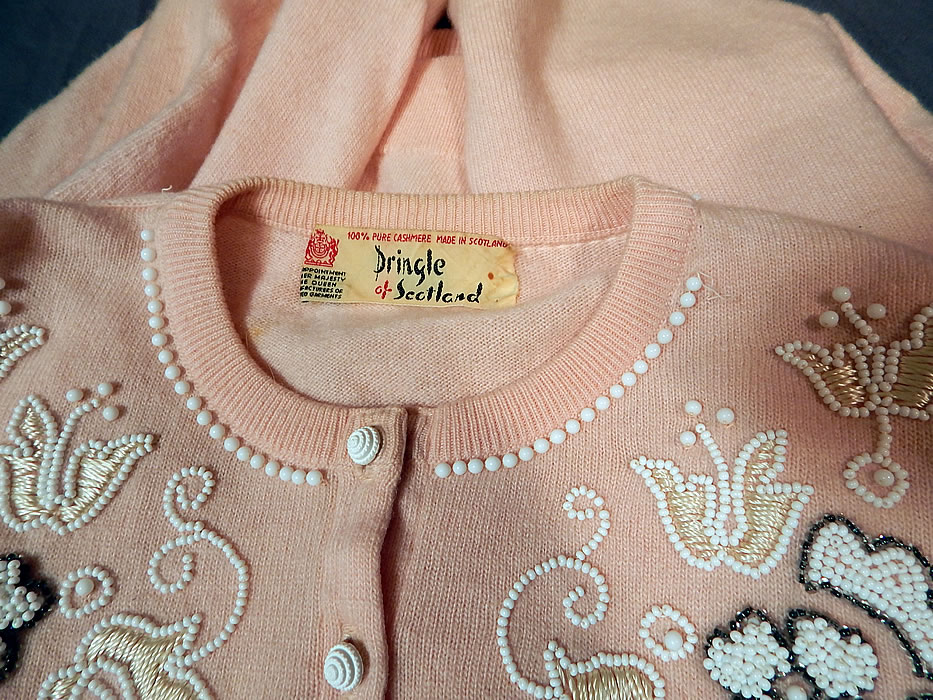 Vintage Pringle of Scotland Pink Cashmere White Beaded Cardigan Sweater
This beautiful beaded cardigan sweater has a ribbed fitted scalloped waistband, cuffs, collar, long full sleeves, unlined and white buttons down the front for closure. 