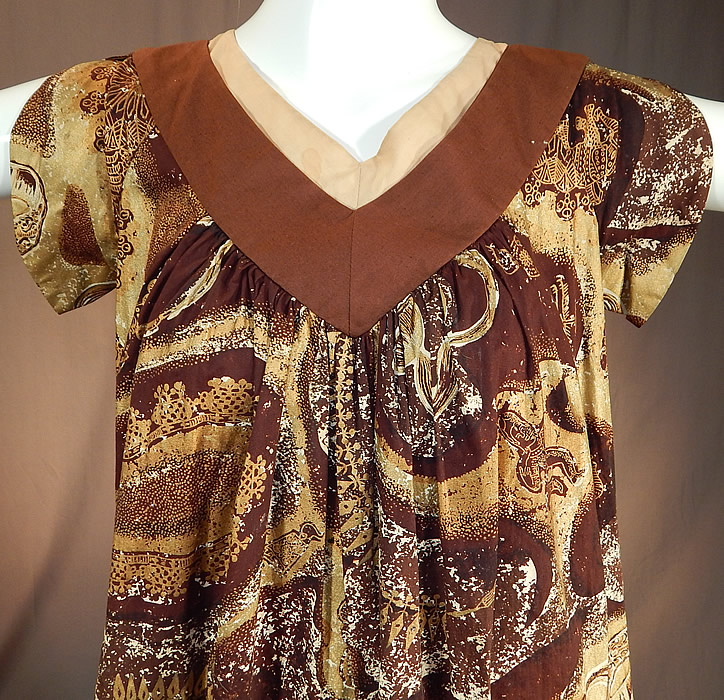 Vintage Watumulls Leilani Hawaii Indonesian Batik Print Gold Cotton MuuMuu Dress
This retro Hawaiian muumuu style shift dress is loose fitting, with a low V back bow tie and neckline trim, short cap sleeves, side pockets and is unlined. 