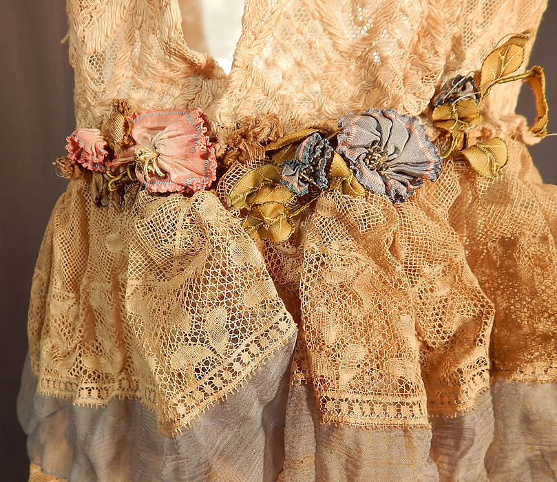 Vintage Cream Tambour Embroidery Lace Silk Rosette Drop Waist Dress
There are colorful pastel silk ombre wired rosette ribbon work flower trim accents around the neckline, hanging down the back tie sash and along the side hip area. This fabulous flapper dress has a loose fitting straight shift chemise style, with a drop waist, an attached blue chiffon necktie scarf with rosette trim ends hanging down the back, sleeveless, with an open side top, no closure, sheer, unlined and a layered tiered ruffle long tea length skirt. 