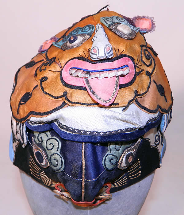Antique Chinese Child Infant Silk Applique Tiger Wind Hat. It is hand stitched, made of colorful silk fabrics, with an appliqu&eacute;d tigers face on the front and on the top, with peaches and flowers appliqu&eacute;d on the sides and back. This unusual animal shaped hand crafted hat has two different detailed 3 dimensional faces of a smiling grinning tiger, with it's ferocious powers make it an especially popular protective image and would have been used to frighten off evil spirits. 