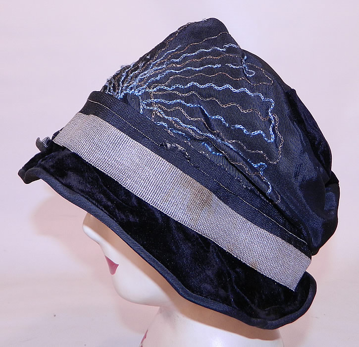 Vintage Dahlia Model Black Silk Velvet Gold Lame Lam&eacute; Embroidered Flapper Cloche Hat. The hat is made of black silk and velvet fabrics, with gold metallic lam&eacute;, blue chain stitch embroidery work trim sunburst on the front crown and a silver lam&eacute; ribbon trim hatband. 