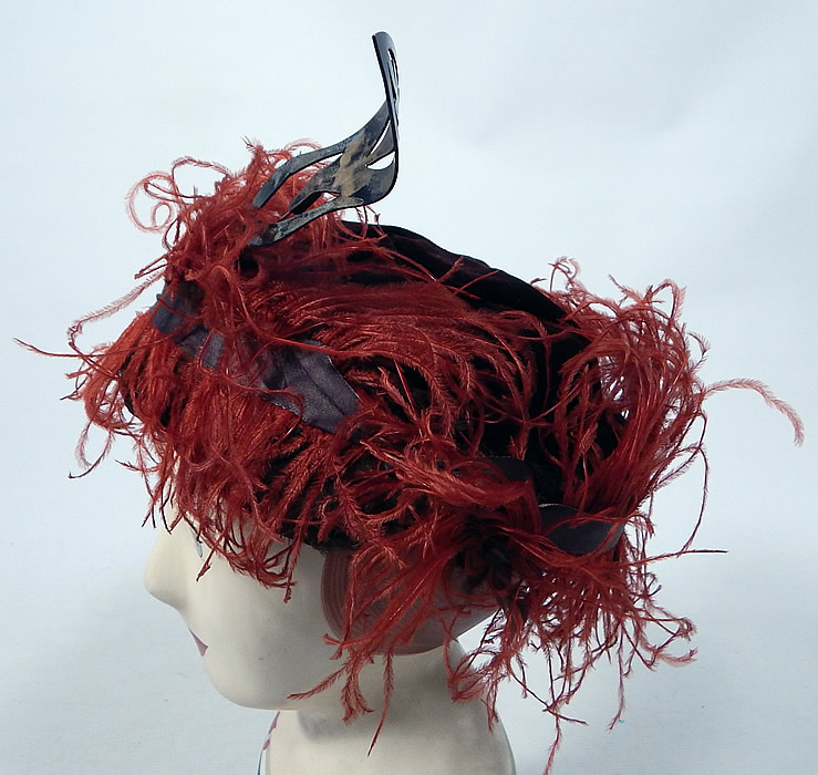 Vintage McGrath Millinery Belle Epoque Burgundy Velvet Feather Trim Toque Hat
The hat is made of a dark red burgundy wine color velvet fabric, with reddish orange ostrich feathers and gold lam&eacute; ribbon trim surrounding it. 