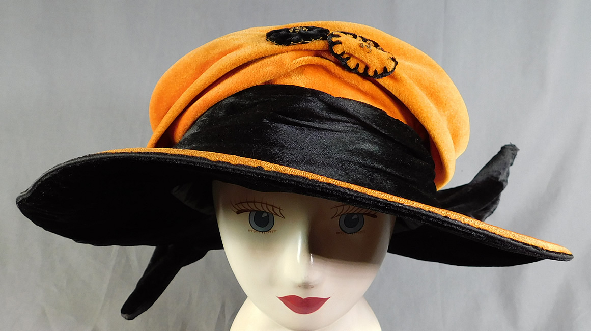 Vintage Harris Hat & Cloak Shop Orange Black Velvet Winged Wide Brim Cloche
The hat is made of a orange and black velvet fabric, with contrasting velvet rosette gold metallic embroidered applique trim on the front crown.