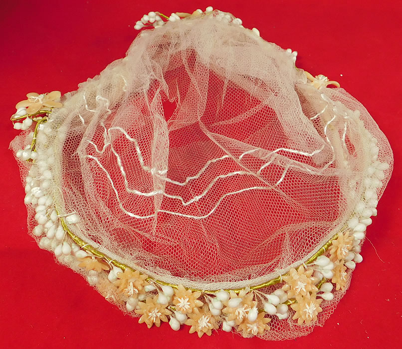 Vintage 1920s Wax Flower Bridal Wreath Wedding Headband Headpiece Juliet Cap 
This vintage flapper wax flower bridal wreath wedding headband headpiece Juliet cap dates from the 1920s. The headpiece is made of a white wax orange blossom flowers and pearl droplets attached to a green wrapped wired base headband. This beautiful bridal garland wreath wedding headpiece has a Juliet cap style sheer tulle net decorative silk stitched back head covering with a double wax flower strand front headband. The headpiece measures 25 inches in circumference. It is in good as-is condition, with only a few missing, broken wax flower petals, droplets and some frays, holes, remnants of the delicate tulle netting in areas. This is truly a wonderful wedding wreath headpiece and wearable flapper bridal art!
