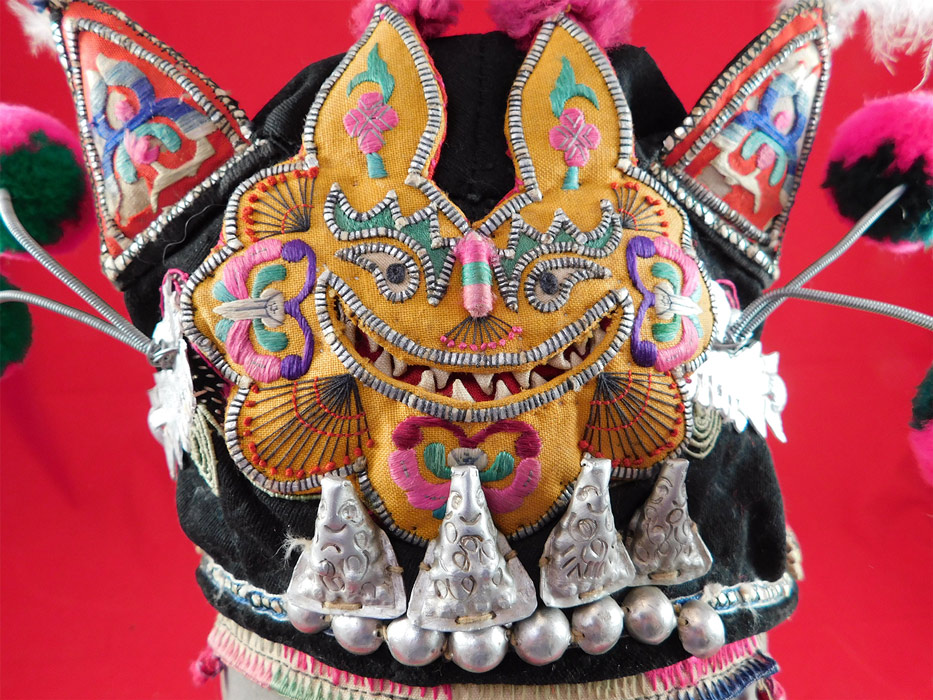 Antique Chinese Bai Miao Minority Childrens Festival Embroidered Tiger Wind Hat
This whimsical children's hat has a yellow detailed raised padded smiling grinning tiger face on the front, with red cat ears trimmed in white feathers on the top, colorful pompom whiskers attached with springs.