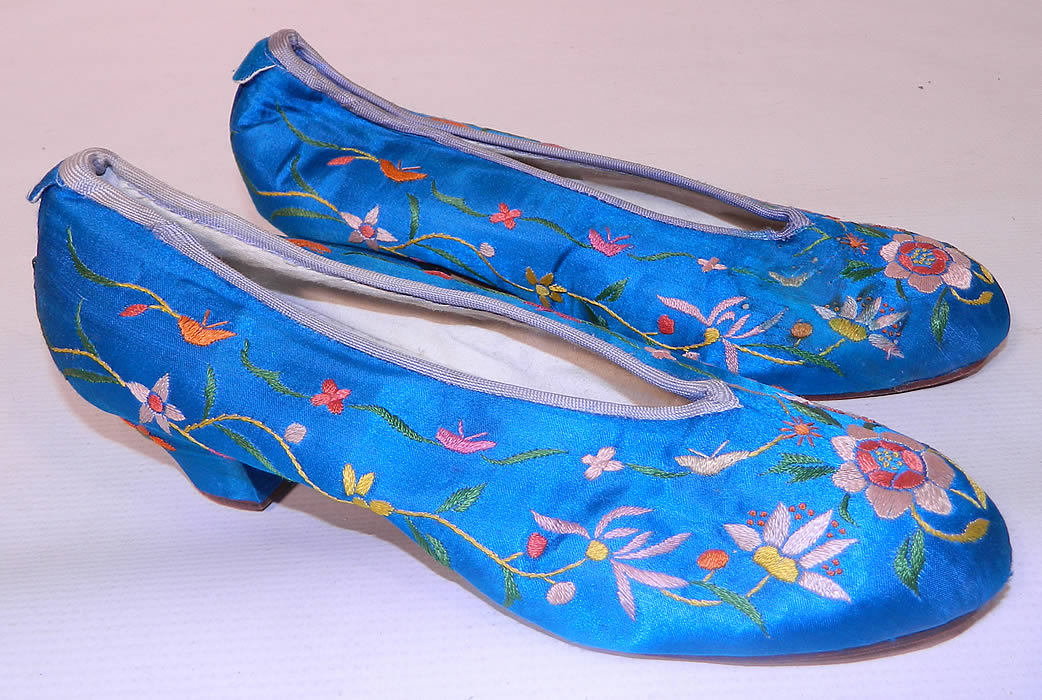 Antique Chinese Royal Blue Silk Embroidered Floral Slipper Shoes. They are made of a bright royal blue color silk fabric, with colorful floral silk raised padded satin stitch embroidery work and a bluish gray silk rope cord trim edging along the top.