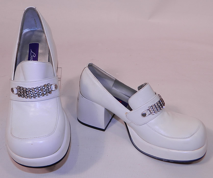 Unworn Vintage Baci Rhinestone Trim White Leather Loafers Disco Platform Shoes. These retro 1970s style Disco shoes have a slip on penny loafer style, with a platform front lift, rounded toes, chunky cube high heels and black rubber grip bottom soles. 