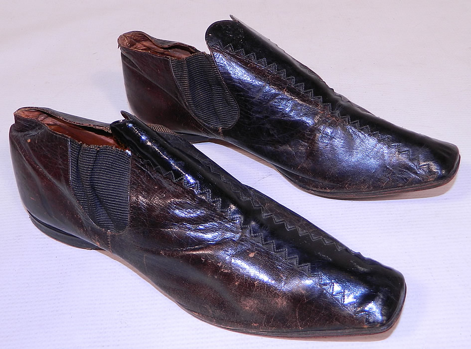 Victorian Brown & Black Leather Crooked Sole Square Toe Dainty Ankle Half Boots
This pair of antique Victorian era brown and black leather crooked sole square toe dainty ankle half boots date from the 1850s. They are made of a dark brown leather, with black patent leather inserts and decorative zig-zag stitching down the front tops.