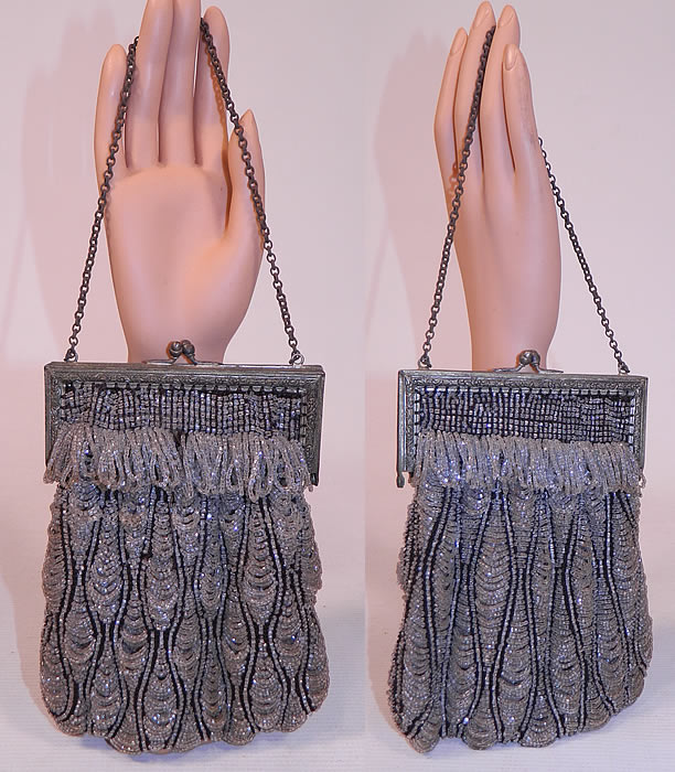 Vintage Art Deco Black Knit Crystal Beaded Loop Fringe Silver Frame Flapper Purse
This vintage Art Deco black knit crystal beaded loop fringe silver frame flapper purse dates from the 1920s. It is made of a black knit fabric covered with crystal hand beading done in a loop fringe layered scalloped design. This fabulous flapper Art Deco handbag purse has a silver metal frame with ball clasp closure on top, silver chain link strap on top for carrying and is fully lined in a beige silk fabric, with gold lam&eacute; metallic pink trim edging inside the top.
