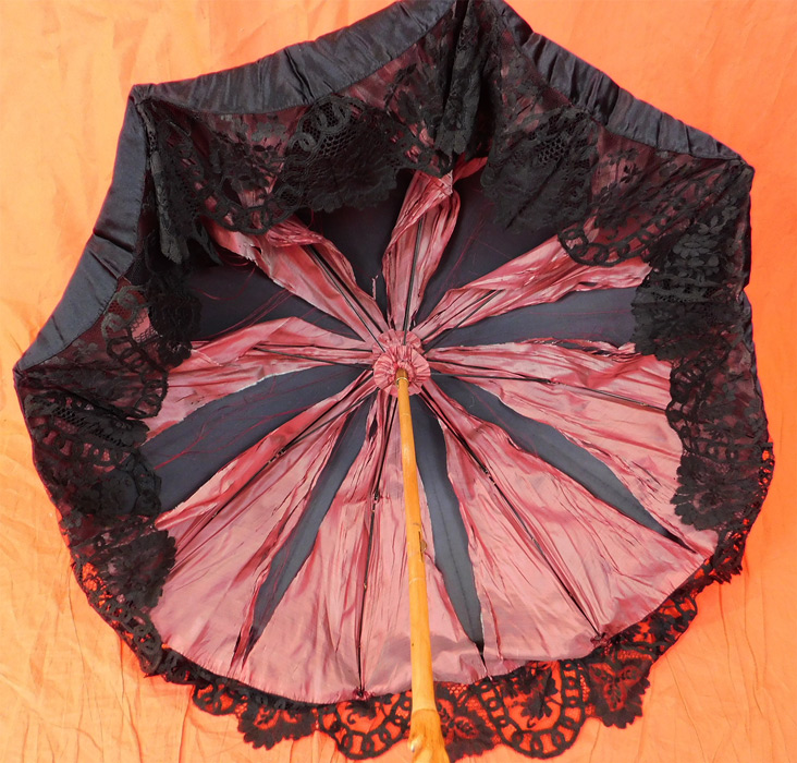 Edwardian Antique Black Silk Lace Burl Wood Stafford Knot Handle Parasol
This pretty parasol has a beautiful natural burl knotted wood handle with a unique Stafford knot twisted pretzel shaped bottom, a wood tip finial top and is lined in a purple silk fabric. 
