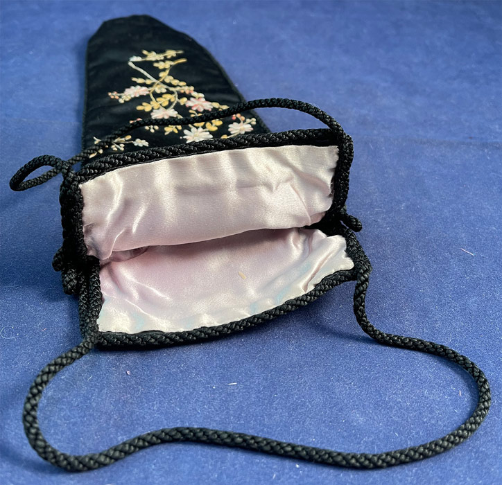 Victorian Silk Rosette Ribbon Embroidery Dragonfly Floral Fan Bag Pouch Purse
This beautiful bag pouch purse has a long slender cone shape coming to a point at the bottom, with an open top, no closure, black silk rope trim edging with double strap for carrying at the top, is fully lined in a pink silk fabric and might have been used to carry a folding hand fan, or small folding parasol. 